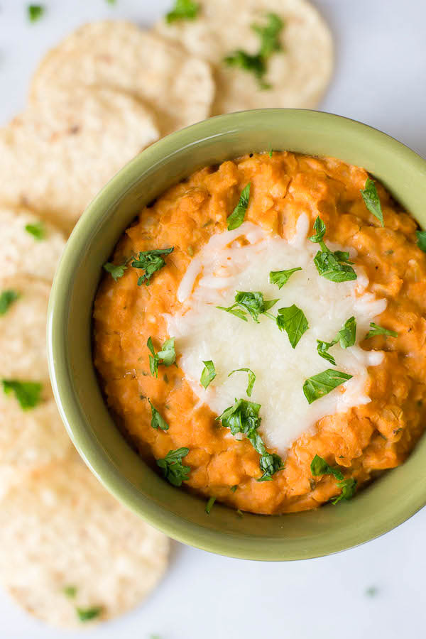 a bowl of buffalo chickpea dip with cheese on top and tortilla chips on the side