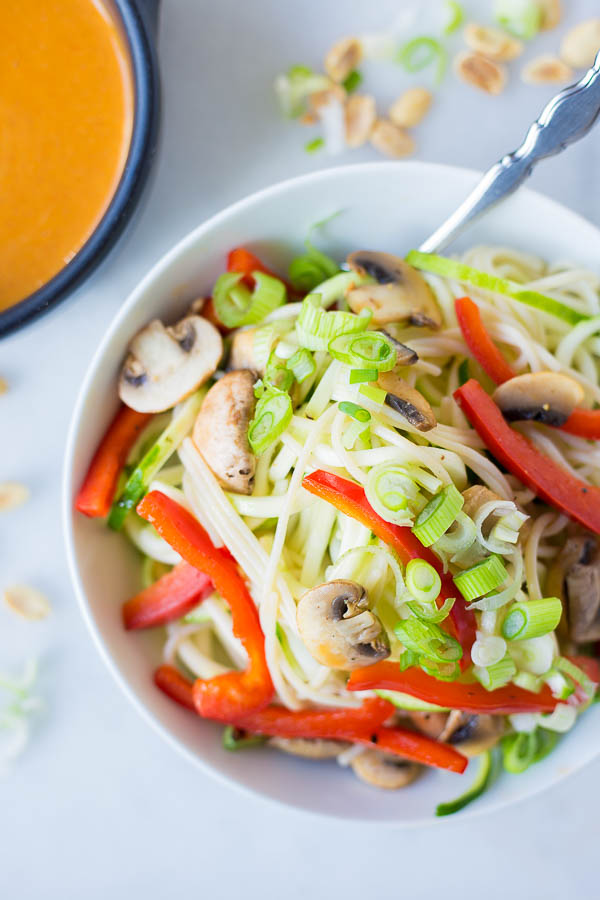 a bowl of noodles, zoodles, and vegetables with peanut sauce on the side