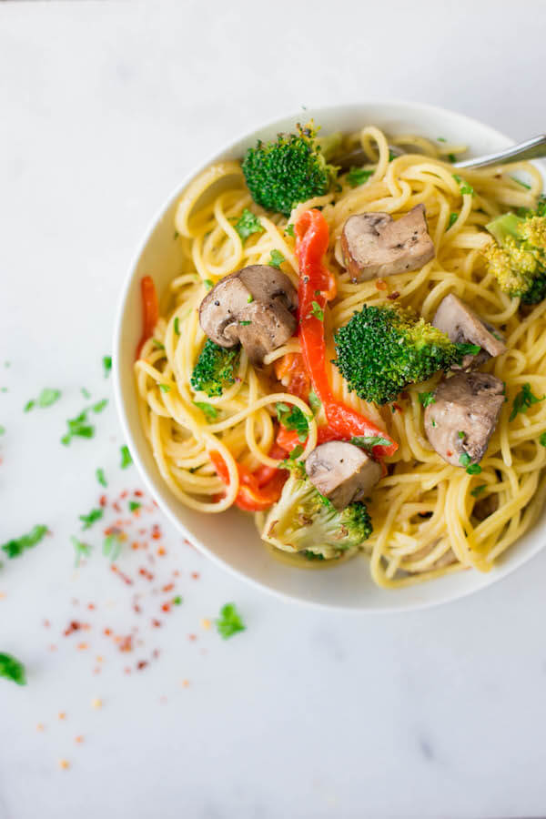 a bowl of creamy lemon hummus pasta with mushrooms, broccoli, and peppers in it