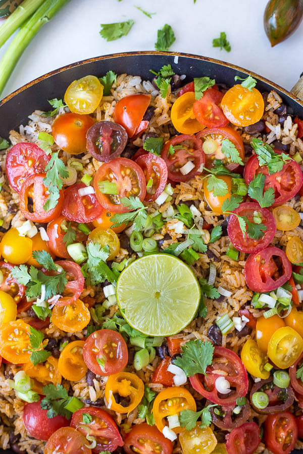 A skillet full of rice, beans, tomatoes, green onion, cilantro, and a lime