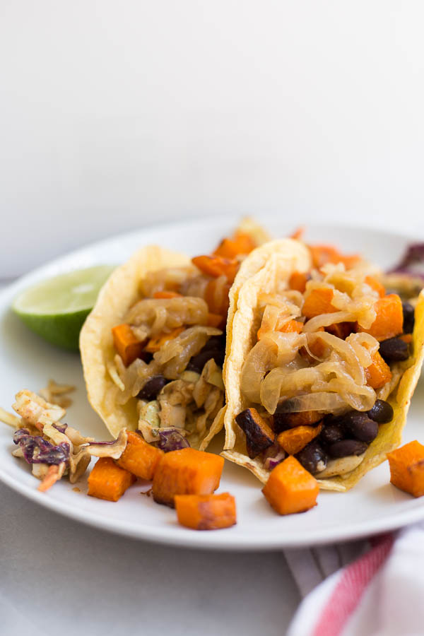 Fall Butternut Squash Tacos: These gluten free and vegan tacos are filled with ingredients like roasted squash, seasoned black beans, hummus slaw, and caramelized onions! An easy and healthy way to enjoy tacos this season! || fooduzzi.com recipe