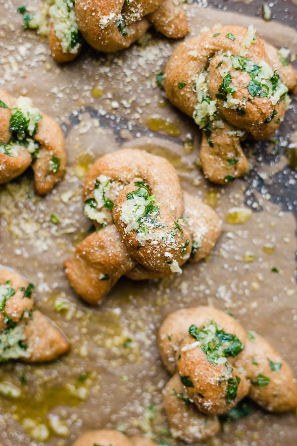 Cheesy Vegan Garlic Knots: Simple, semi-whole wheat garlic knots made vegan and sprinkled with vegan parmesan cheese! Seriously one of the easiest homemade bread recipes you'll ever make! || fooduzzi.com recipe #garlic #homemadebread #vegan