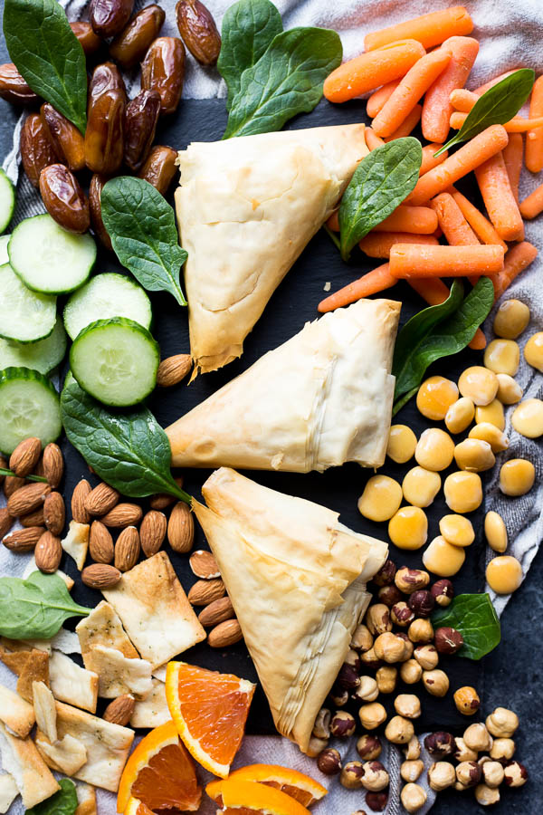 spanakopita on a board with nuts, fruits, and veggies