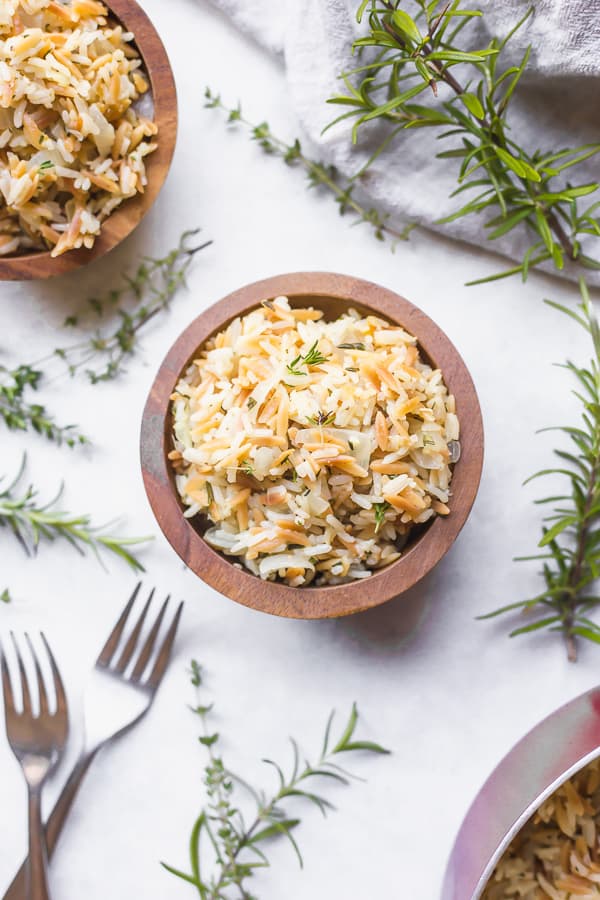 two bowls of garlic & herb rice pilaf with forks and herbs