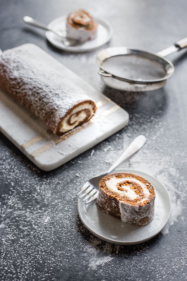 slices of vegan pumpkin roll on plates with forks and a fine-mesh sieve