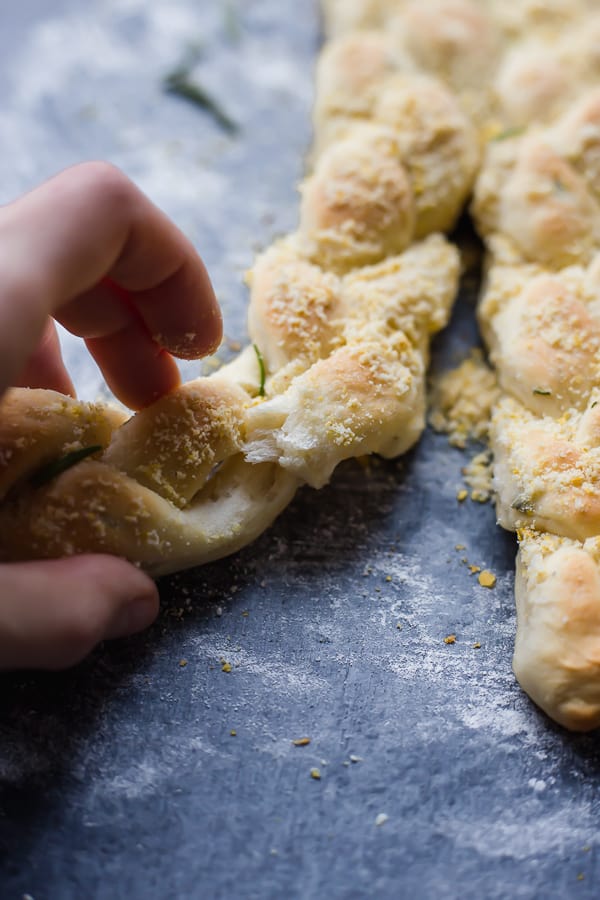 a hand pulling apart a braided rosemary parmesan breadstick