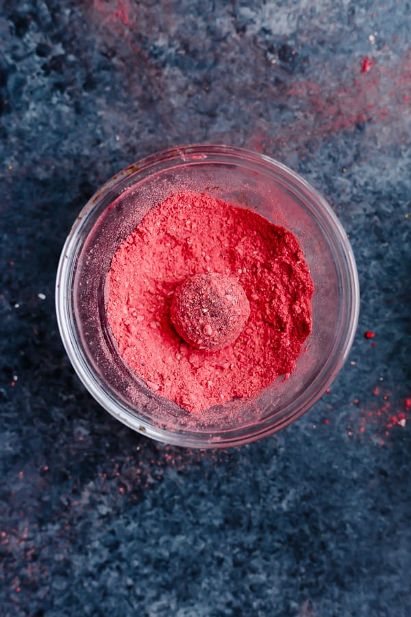 a vegan strawberry chocolate truffle in a bowl of strawberry dust