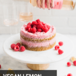 a vegan raspberry lemon cake on a cake stand with a girl pouring wine in the background