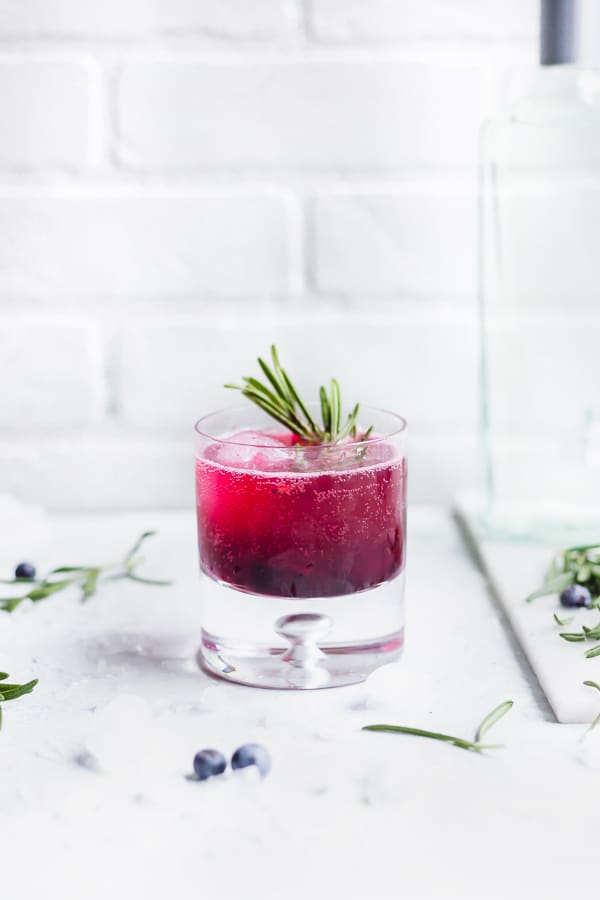 A cocktail glass of the Army of the Dead Blueberry Gin Fizz with a sprig of rosemary