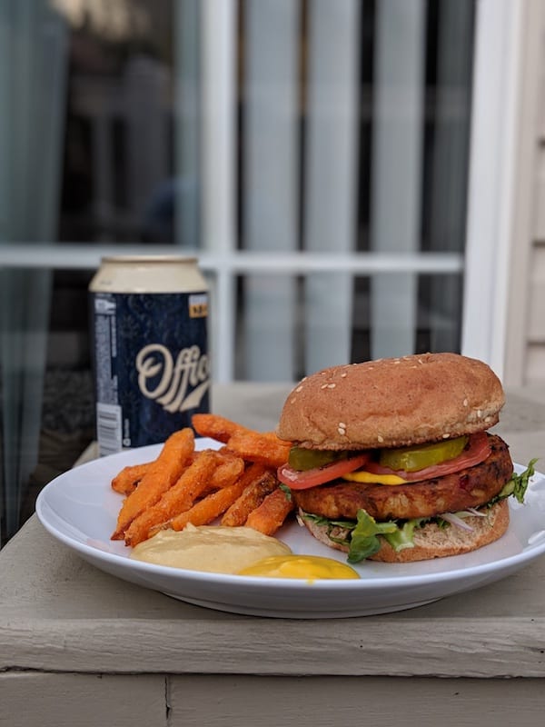 A veggie burger with sweet potato fries and a beer on a table