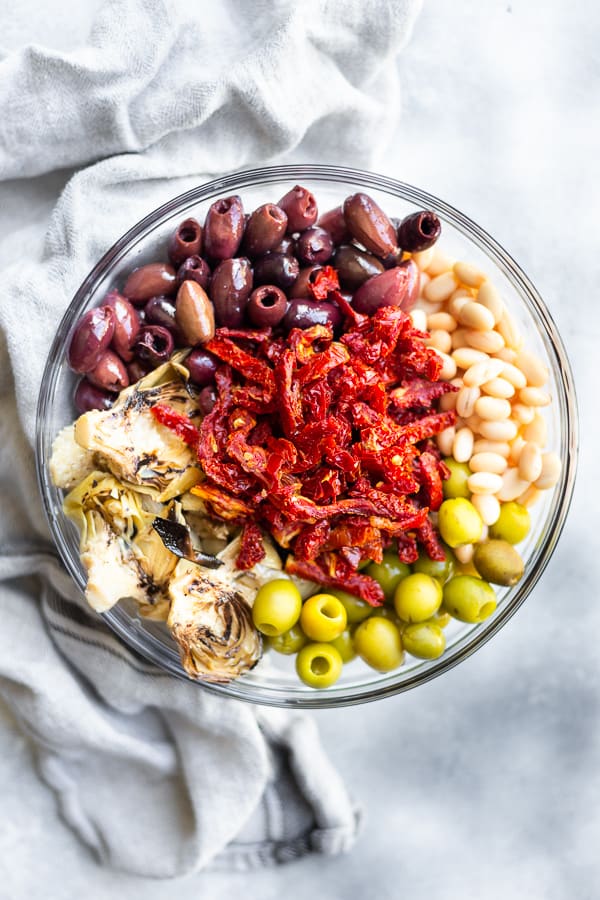 a bowl of olives, sun dried tomatoes, artichokes, and white beans