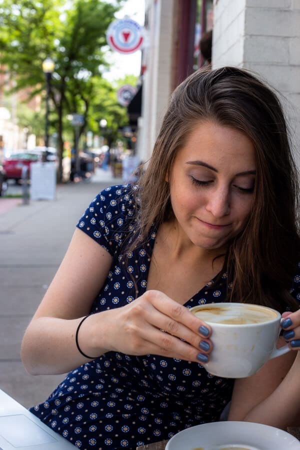 girl drinking a coffee out of a white coffee cup on a street