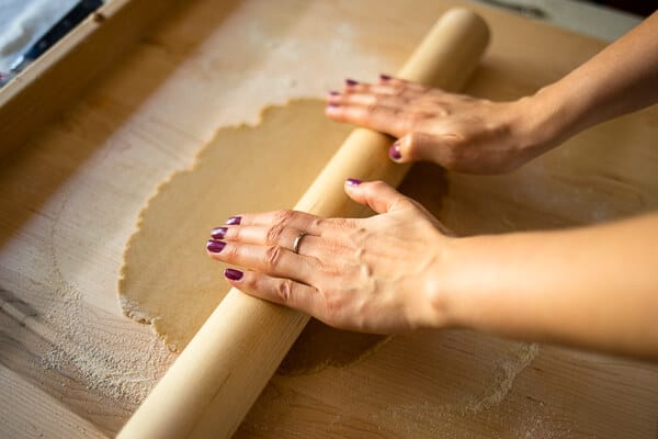 two hands rolling pasta dough on a wooden surface