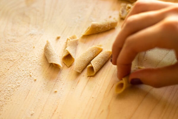 Hand rolling homemade garganelli on a wooden surface