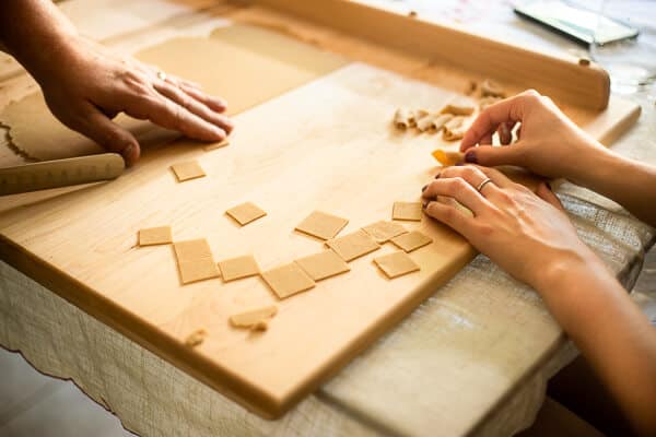 Hand cutting a sheet of pasta dough and two hands rolling homemade garganelli