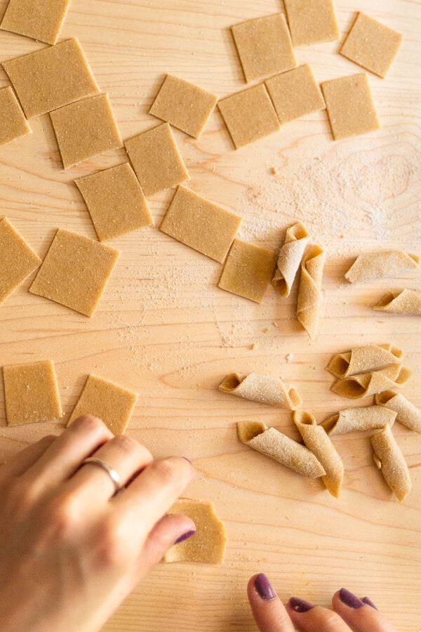 a hand folding squares of homemade pasta dough into garganelli