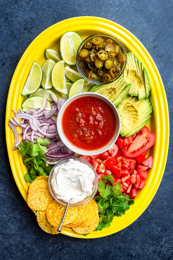a yellow serving platter with mexican toppings like red onion, salsa, jalapeno, and avocado