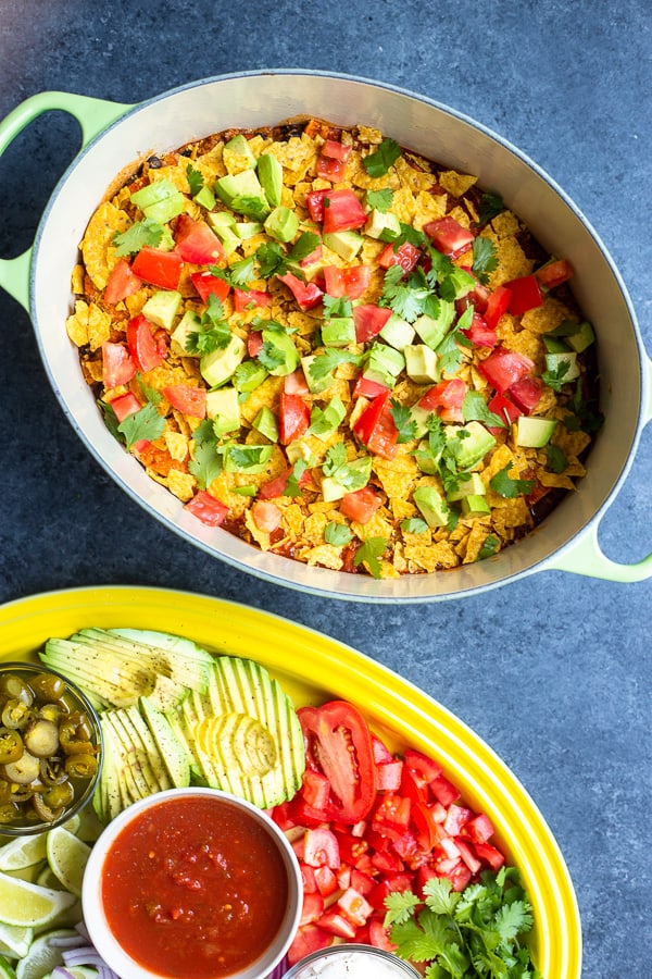 an oval dutch oven filled with a one-pot vegan enchilada casserole and a serving platter with mexican toppings