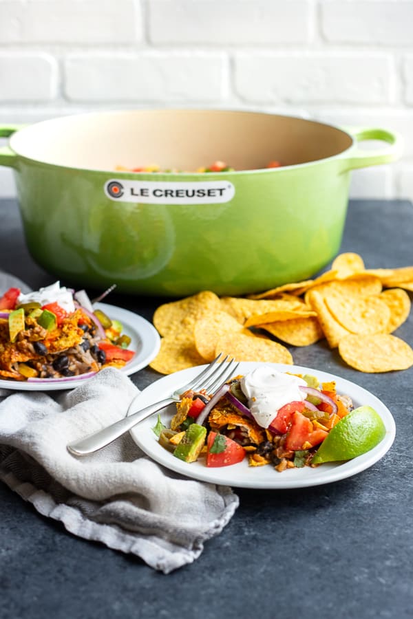 a Le Creuset oval dutch oven with two plates of the One-Pot Vegan Enchilada Cassrole
