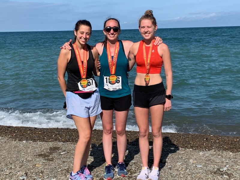 three girls on a beach with medals from a half marathon