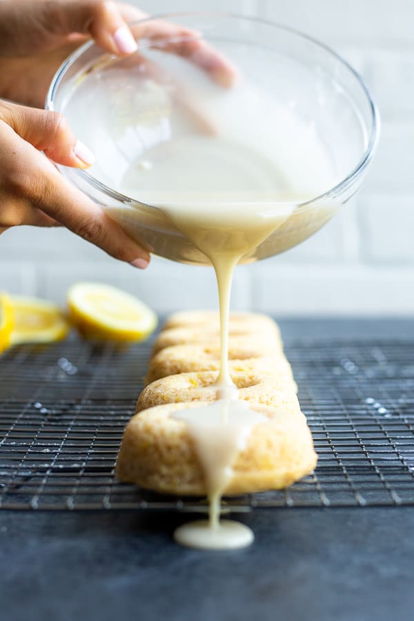 two hands pouring glaze over baked lemon vegan donuts