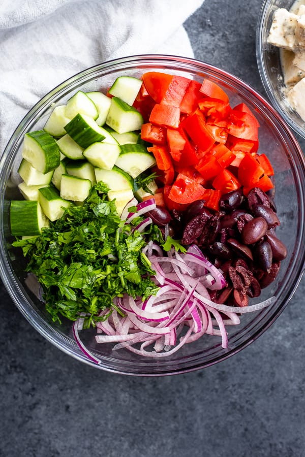 A bowl of chopped tomatoes, cucumber, parsley, red onion, and kalamata olives