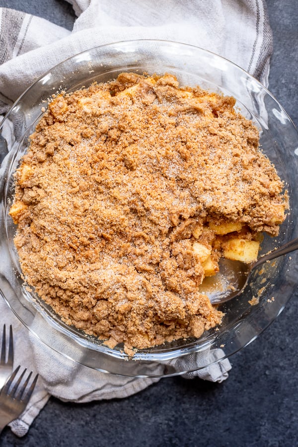 Snickerdoodle Apple Crisp in a pie plate on top of a linen with a spoon