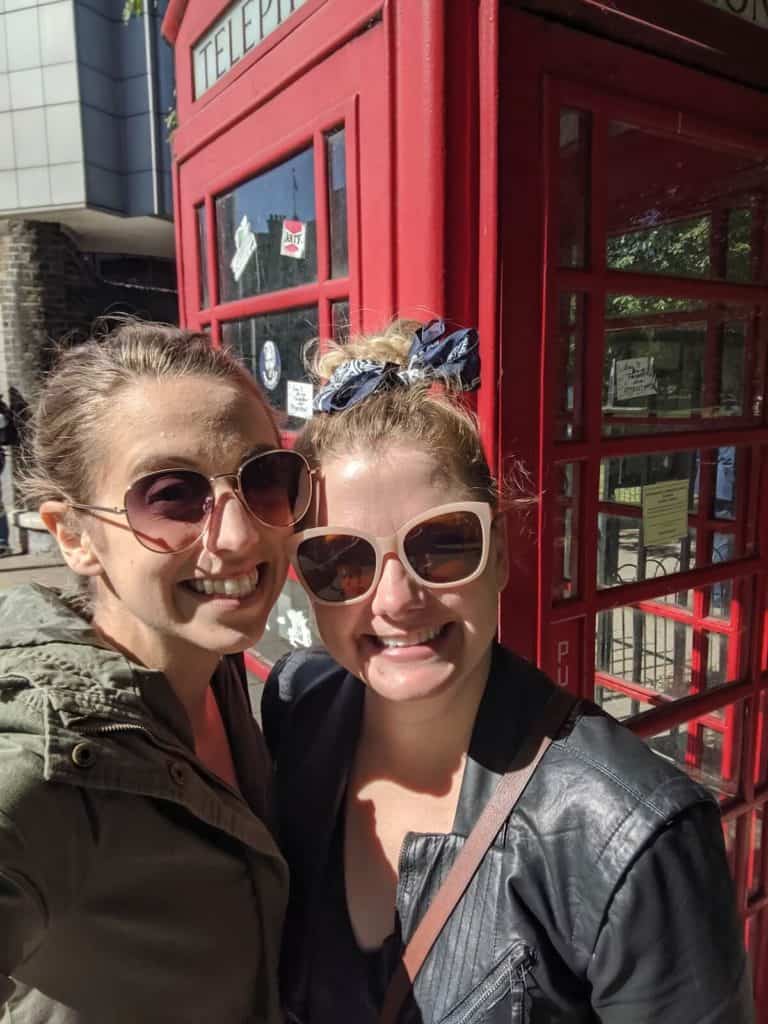 a selfie of two girls in front of a red telephone booth in London