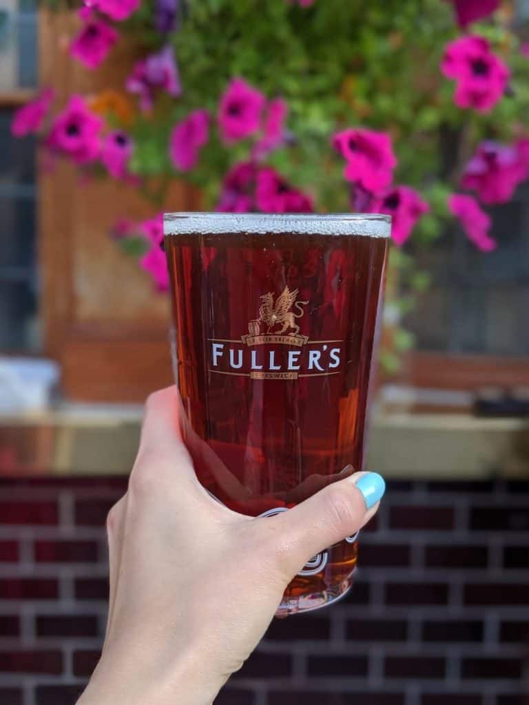 A hand holding a glass of Fuller's ESB at Churchill Arms in London