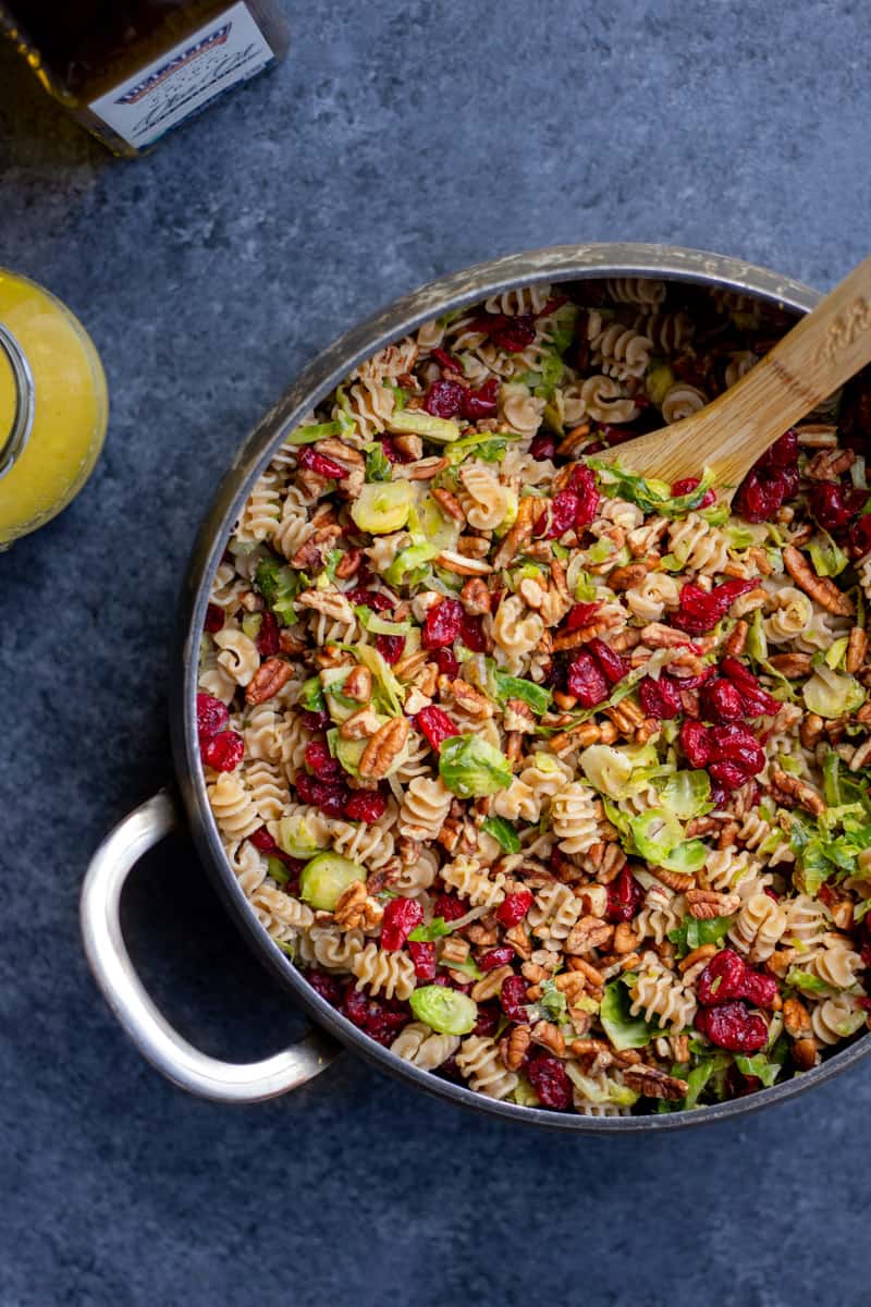Vegan Fall Pasta Salad in a pot with a wooden spoon and dressing off to the side
