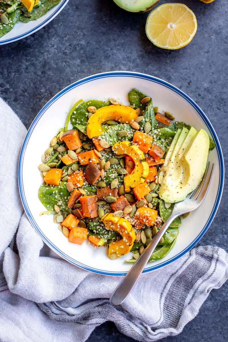 a lemon tahini kale squash salad in a bowl with a fork and a towel underneath