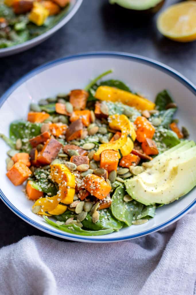 a bowl of the lemon tahini kale squash salad with another bowl of salad in the background