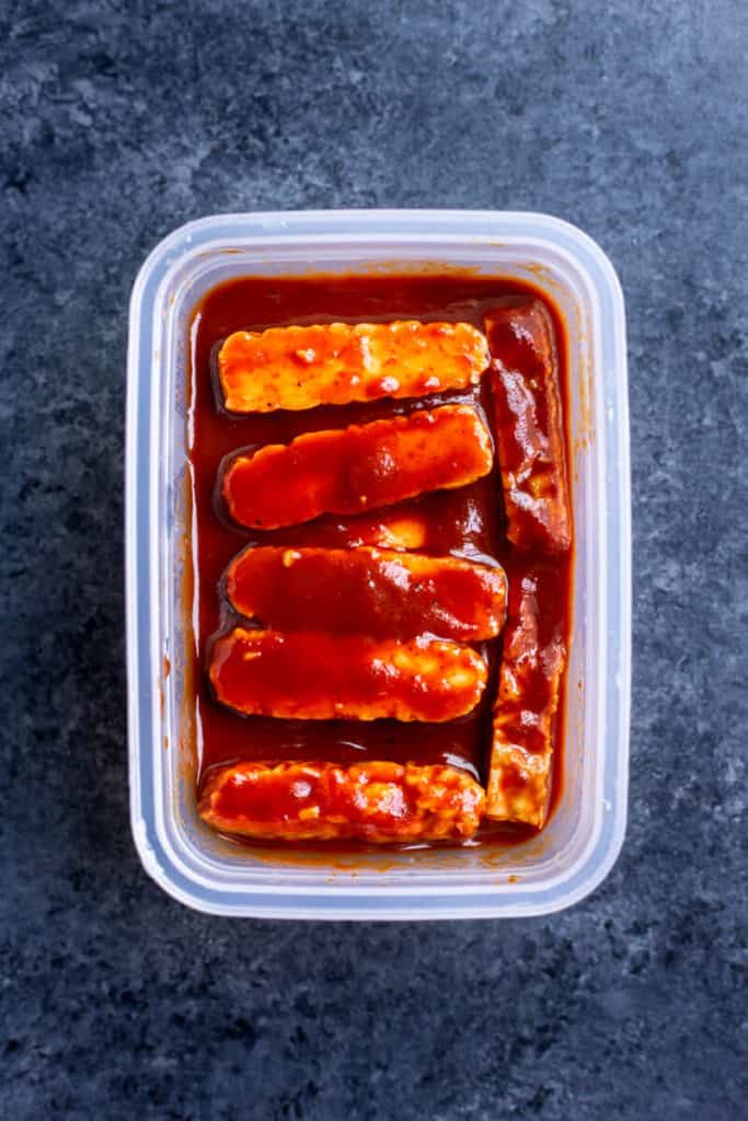 Sliced BBQ Tempeh marinating in BBQ sauce in a container