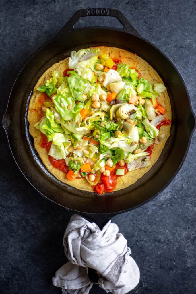 A salad on top of a socca flatbread inside a cast iron skillet