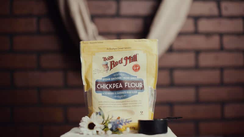 A bag of Bob's Red Mill Chickpea Flour with a measuring cup and flowers in front
