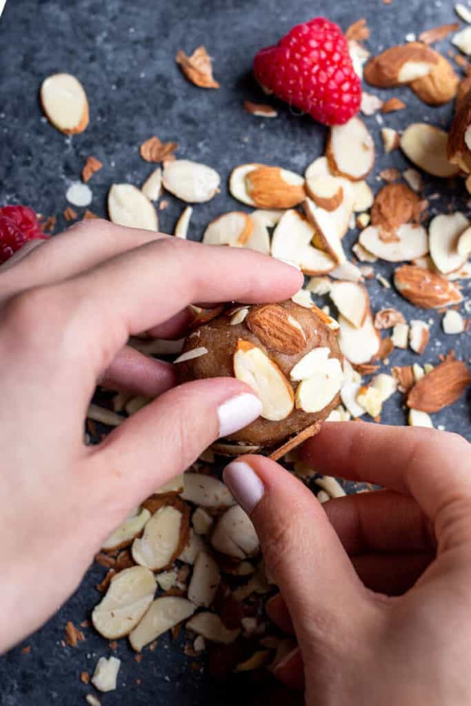 Two hands fixing adding sliced almonds to a Raspberry Almond Date Truffle