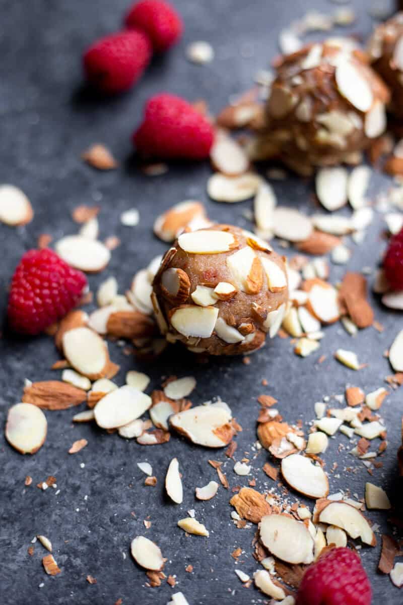 a Raspberry Almond Date Truffle covered in sliced almonds with raspberries and almonds beside it T