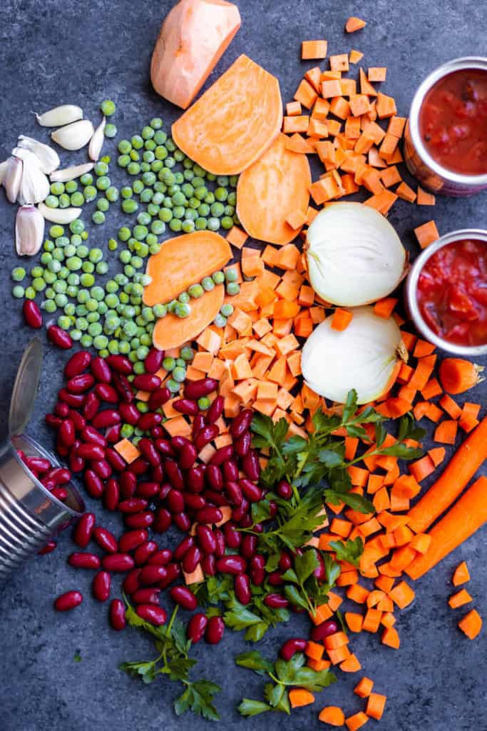 A flat-lay of vegetable soup ingredients like kidney beans, sweet potatoes, peas, onion, and carrots