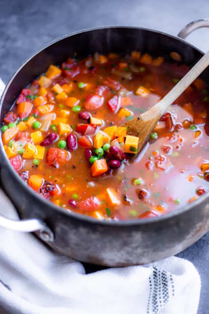 A pot full of vegetable soup with a spoon sticking out of it