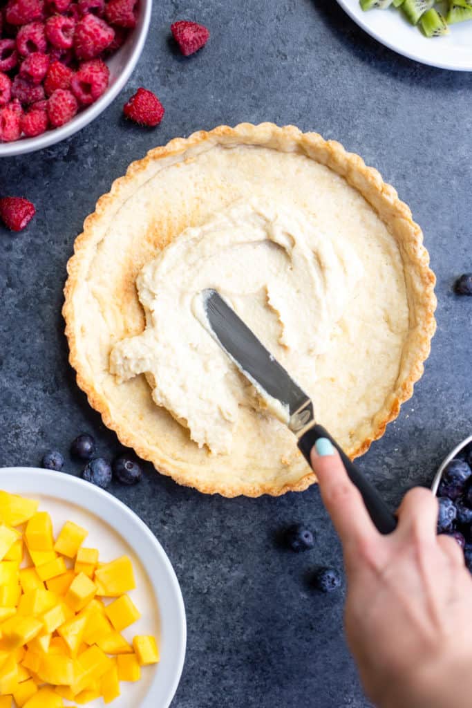 a hand spreading vegan cream cheese frosting onto a tart crust