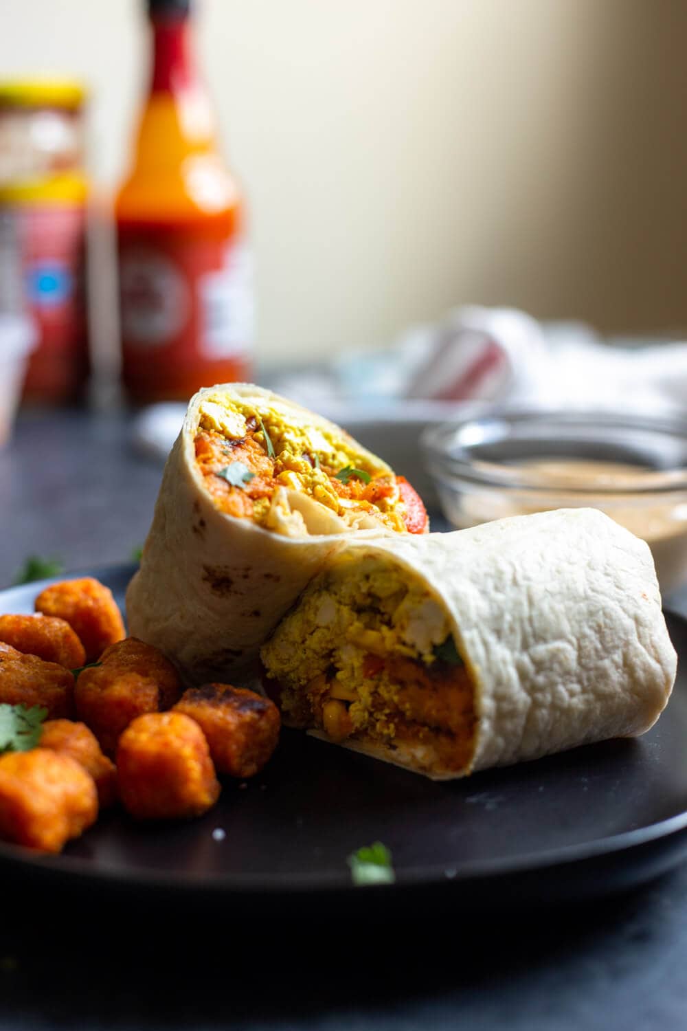 a sliced vegan breakfast burrito on a plate with tater tots on the side