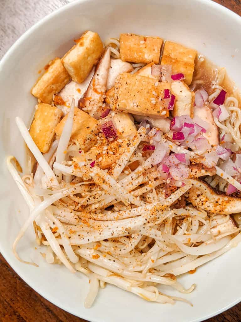 a bowl of vegan ramen with tofu, bean sprouts, and onion