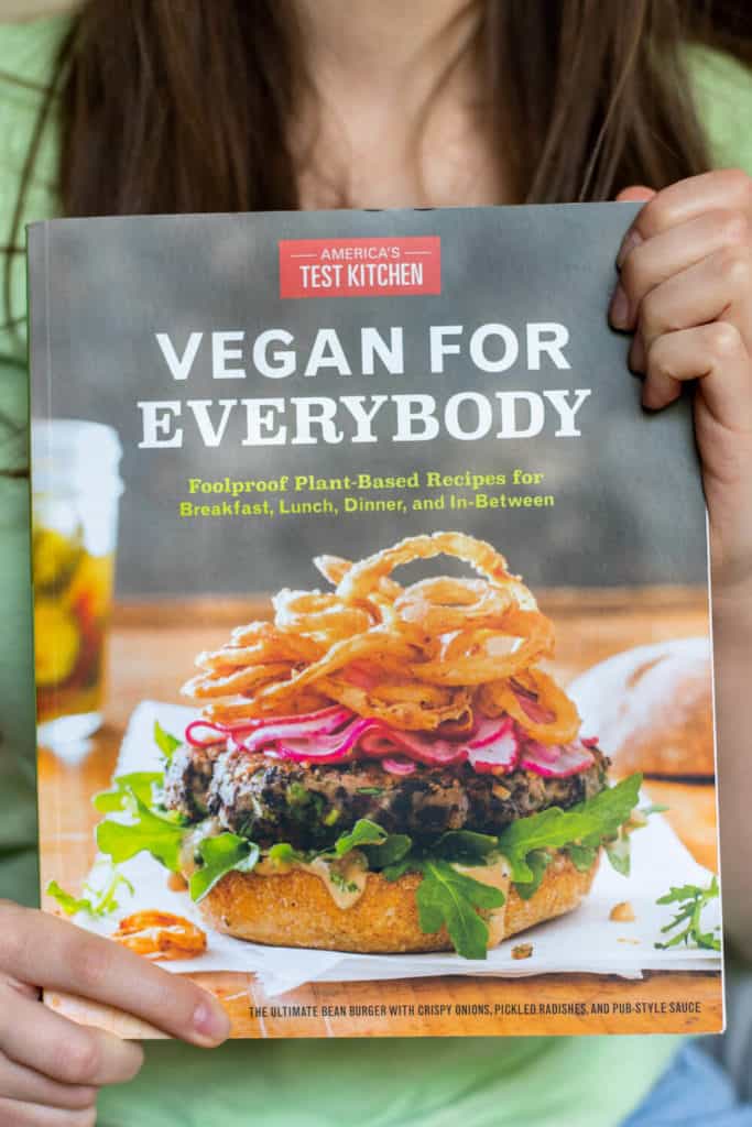 a girl holding America's Test Kitchen's 'Vegan for Everybody' cookbook