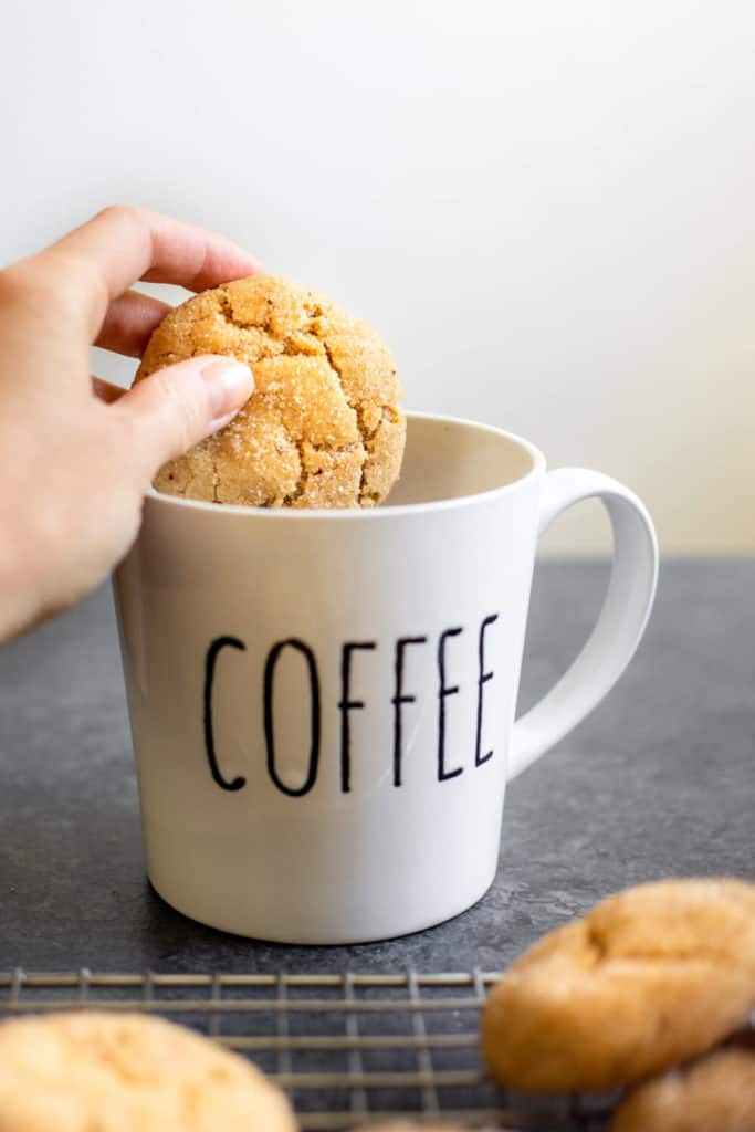 a hand dipping a vegan maple pumpkin spiced snickerdoodle in a mug of coffee