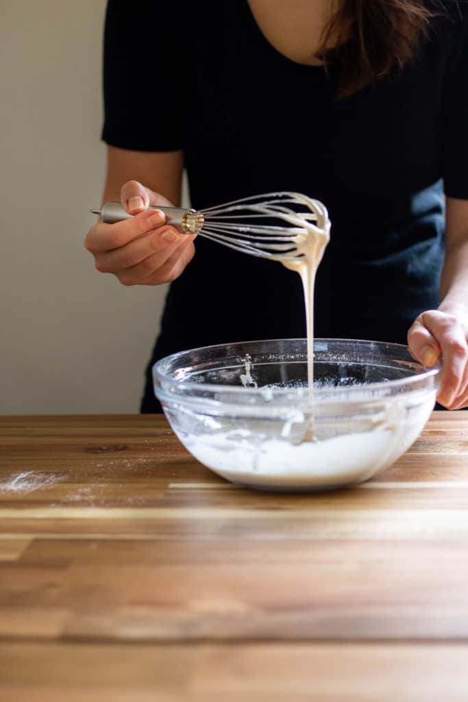 A girl holding a whisk with vanilla bean glaze dripping off