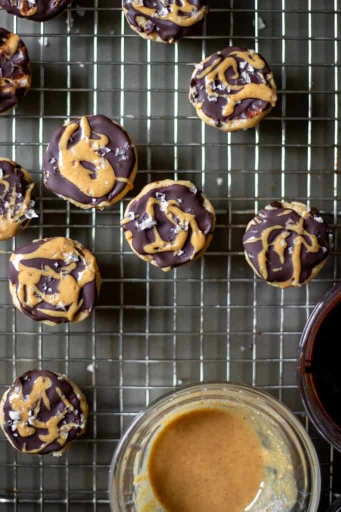 vegan chocolate peanut butter cookie dough bites on a cooling rack with a bowl of melted peanut butter in the corner