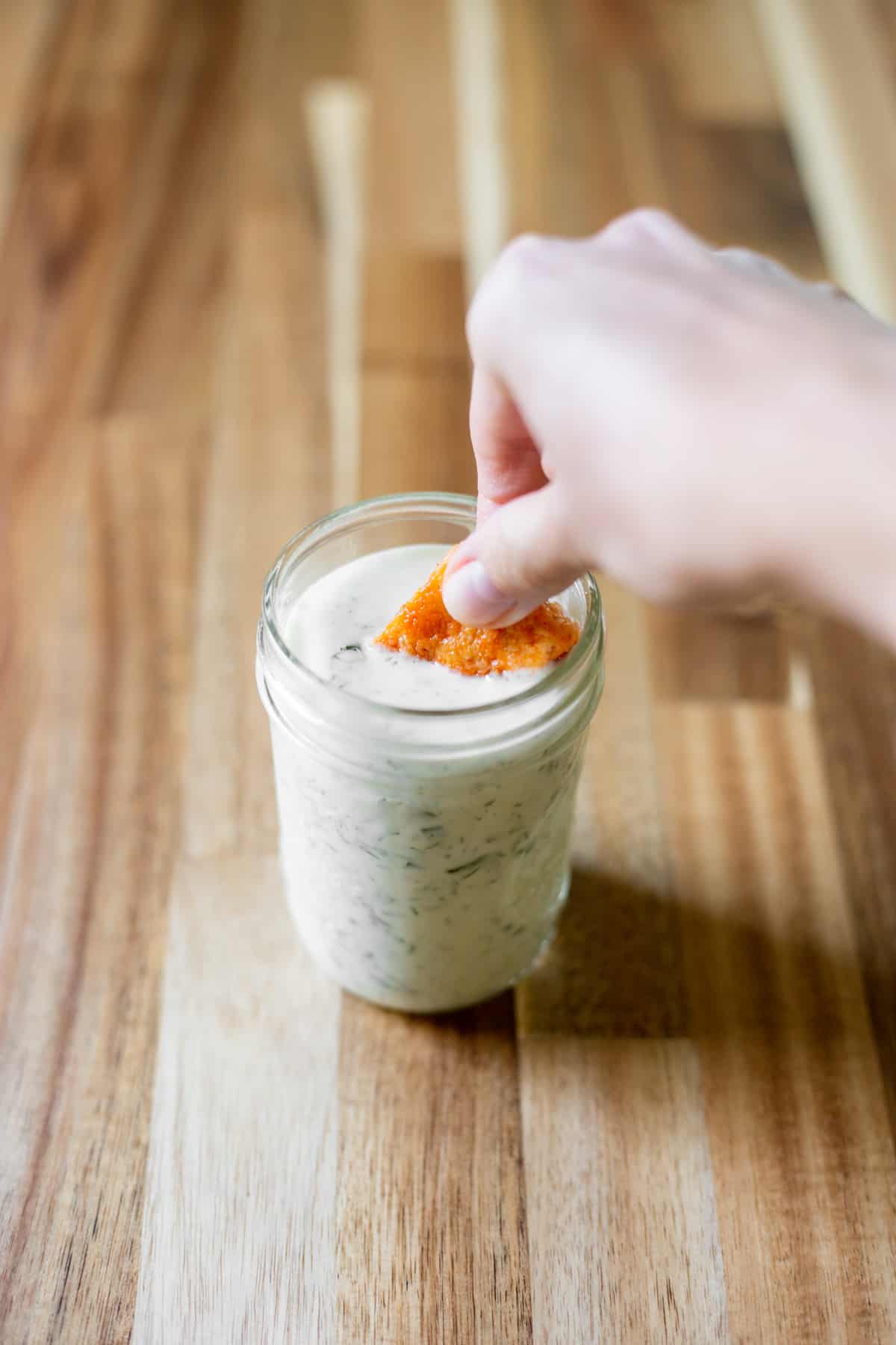 a hand dipping buffalo tofu into a jar of vegan herby ranch