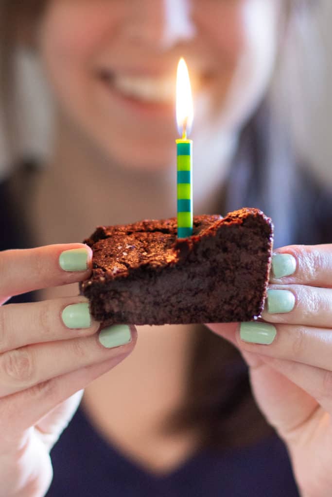 a girl holding a vegan peanut butter cup brownie with a lit candle on top