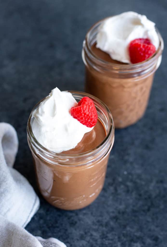 two vegan chocolate peanut butter pots de creme with vegan whipped cream and raspberries on top