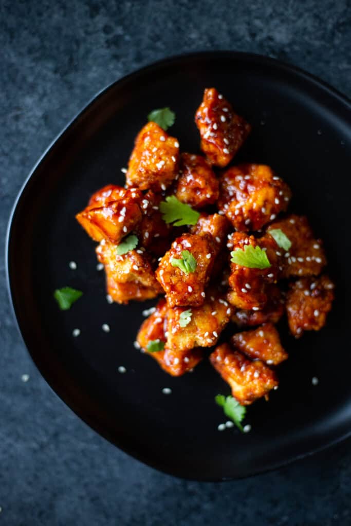 gochujang maple tofu nuggets on a black plate topped with cilantro and sesame seeds
